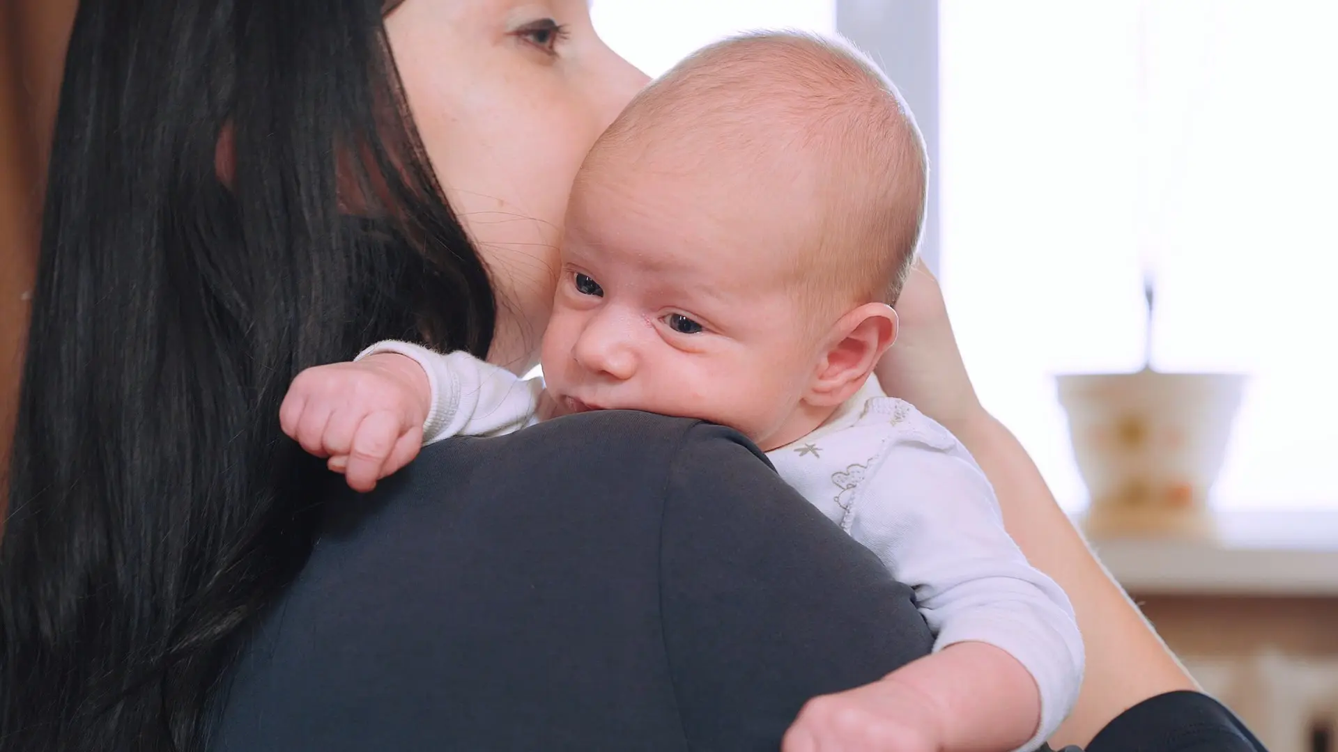 Mother kissing newborn baby on shoulder